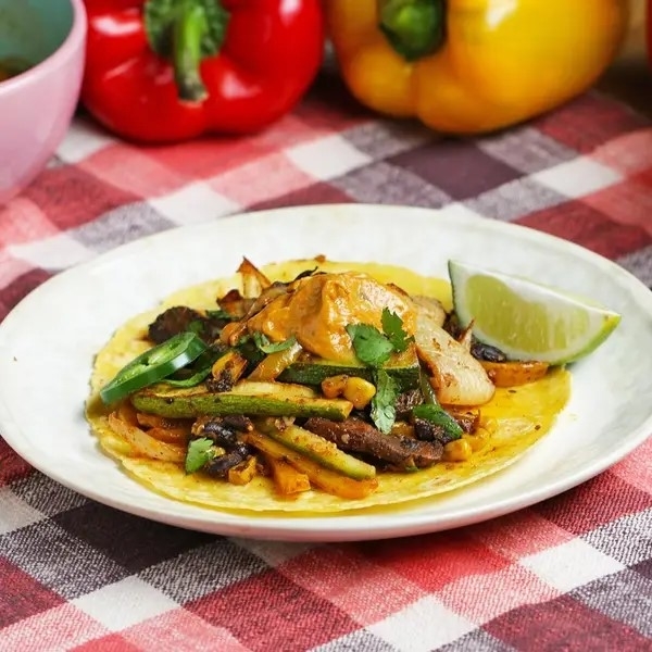 Plate with tacos, grilled vegetables, and a lime wedge on a checkered tablecloth