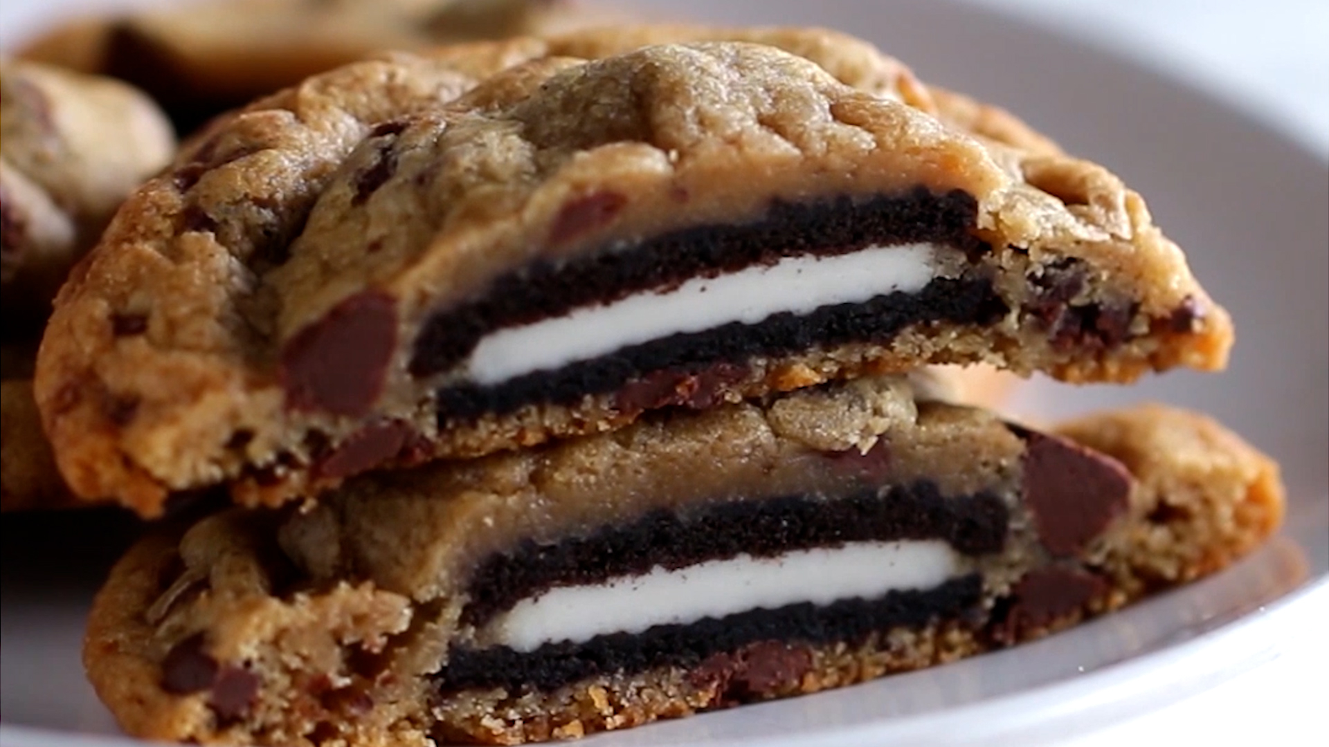 A close-up of a chocolate chip cookie split in half, revealing a whole Oreo cookie baked inside