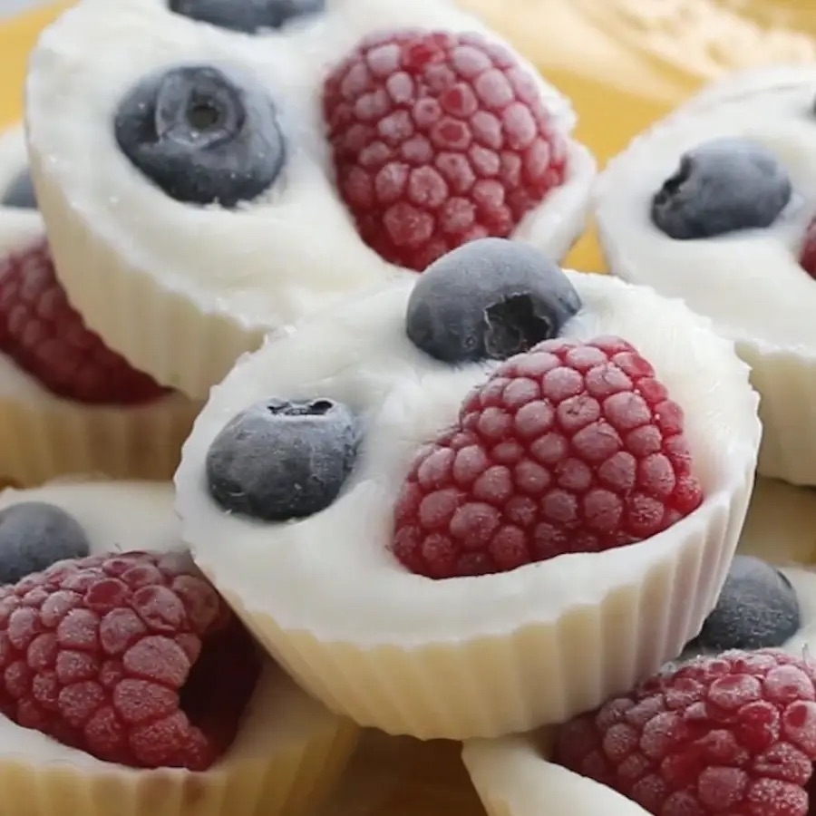 Frozen yogurt cups with whole blueberries and raspberries are displayed close together on a yellow surface