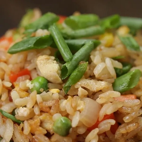 A close-up image of a delicious serving of fried rice with green beans, peas, and diced chicken