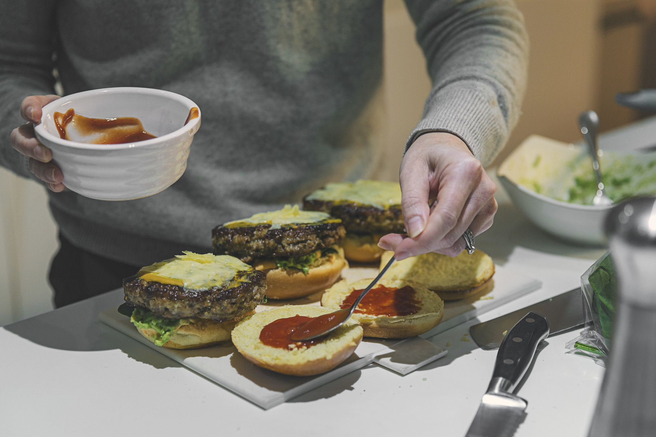 A person putting condiments on homemade hamburgers