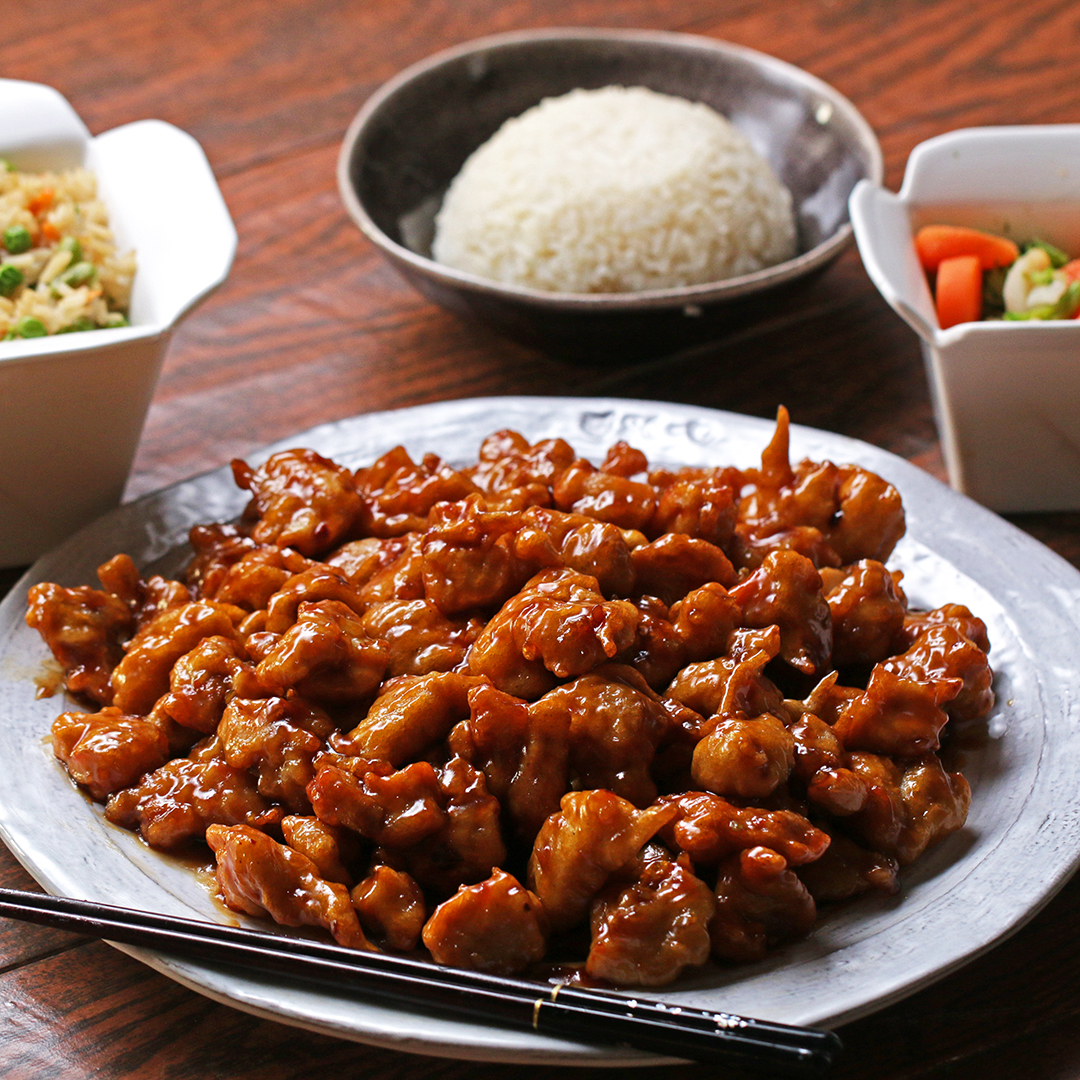 Plate of sweet and sour chicken with chopsticks, steamed white rice, fried rice, and a side of mixed vegetables