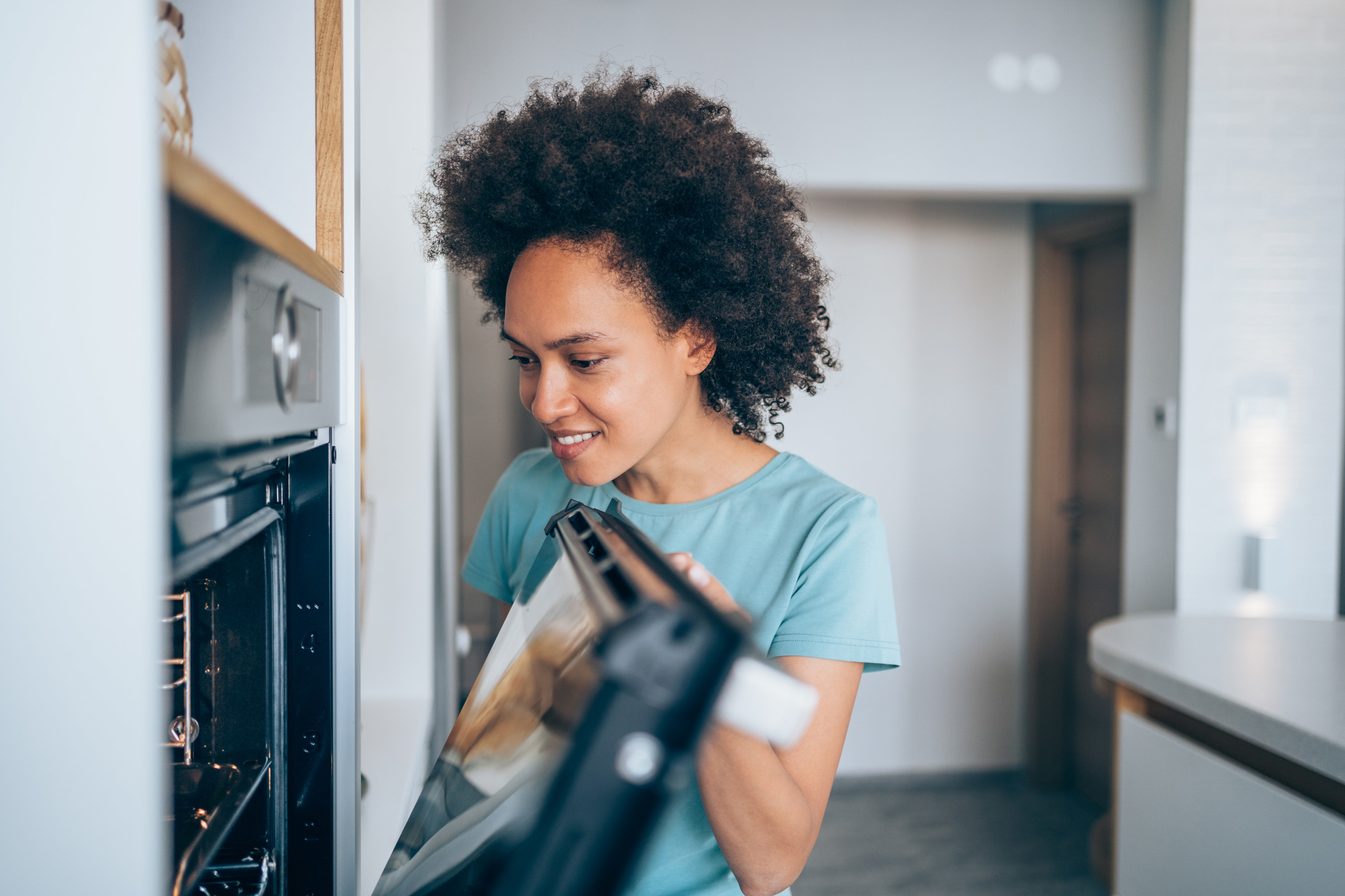 Smiling woman checking food in the oven.