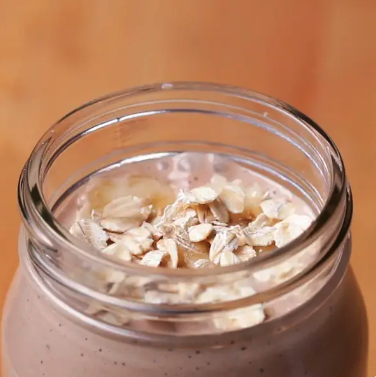 A glass jar filled with a smoothie topped with oats and banana slices